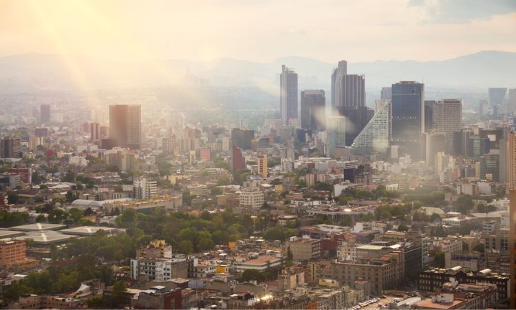 Rascacielos iluminados se alzan; el sol brilla sobre una vibrante ciudad moderna, destacando edificios y espacios verdes en un entorno urbano.