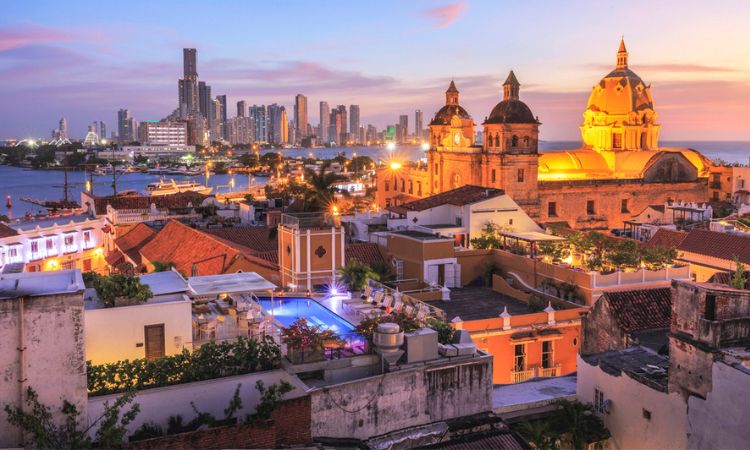 Edificios históricos iluminados al atardecer en una ciudad costera; horizonte urbano moderno al fondo. Marketing turístico, arquitectura, fotografía urbana.