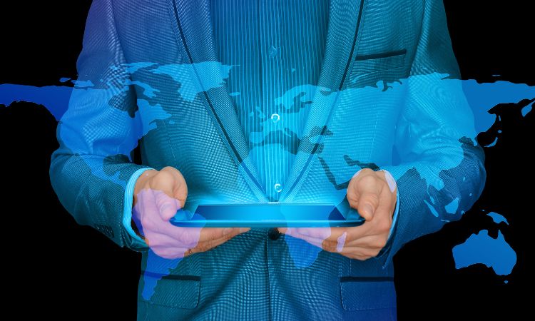 Persona sostiene una tableta proyectando un mapa mundial azul; fondo oscuro. Ideal para temas de marketing digital y globalización.