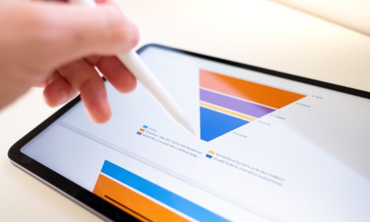 Tableta mostrando un gráfico triangular interactivo; mano con lápiz táctil señala secciones. Contexto de análisis de datos visual en entorno de oficina.