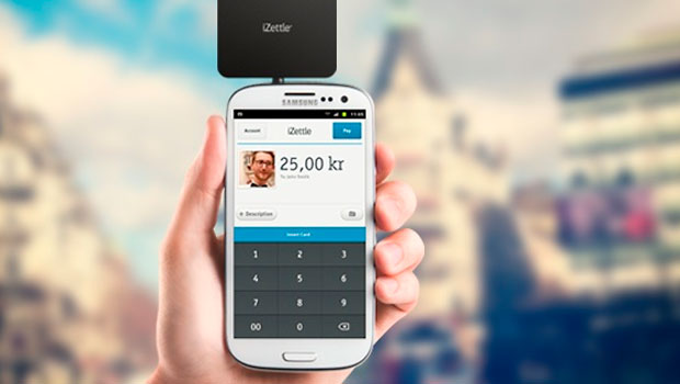 Mano sostiene un smartphone con un lector iZettle, mostrando el pago de 25,00 kr, en un entorno urbano desenfocado. Marketing móvil.