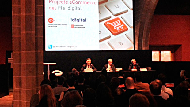 Presentadores sentados en una mesa hablan ante una audiencia en un evento de eCommerce, con diapositivas proyectadas sobre el Pla digital de Cataluña. Texto: "Proyecte eCommerce del Pla idigital", "Consell General de Cambres de Catalunya", "idigital Generalitat de Catalunya", "@cambra­­_com #digitalocom".