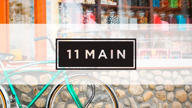 Bicicleta estacionaria frente a escaparate con frascos coloridos, texto "11 MAIN" sobrepuesto. Ambiente de tienda local vibrante, atrayendo atención.