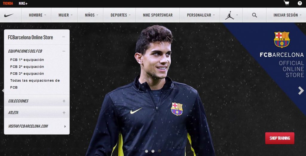 Persona sonriente con chaqueta del FCB bajo lluvia. Menú: equipaciones FCB, colecciones, Atleta. Texto: "FCBarcelona Online Store", "SHOP TRAINING". Contexto de tienda deportiva en línea.