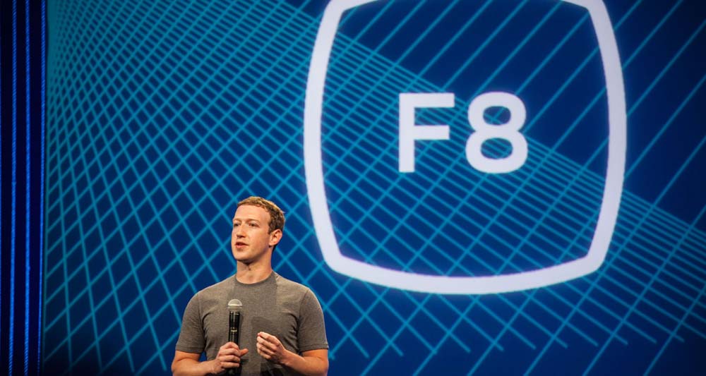 Persona con micrófono habla frente a fondo azul con diseño de cuadrícula y texto "F8", simbolizando evento tecnológico y marketing digital.