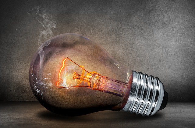 Bombilla iluminada y humeante sobre una superficie gris, simbolizando innovación y creatividad en un contexto de ideas brillantes y descubrimiento.