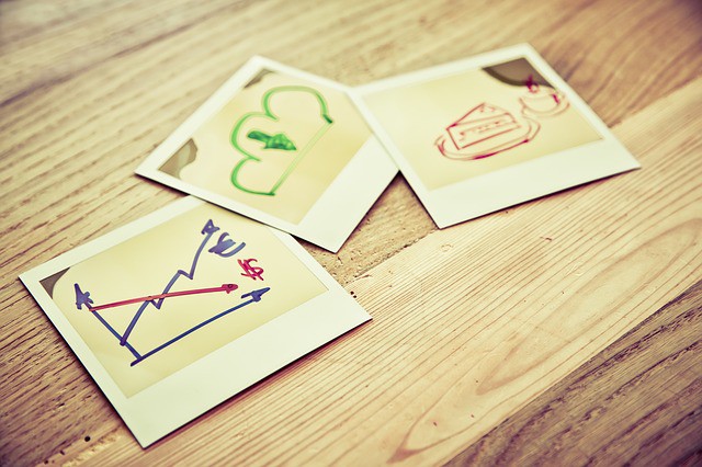 Fotos polaroid muestran dibujos de gráficos y símbolos económicos sobre una mesa de madera, sugiriendo estrategias y análisis financiero.
