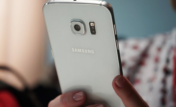 Teléfono Samsung siendo sostenido por una mano, con fondo desenfocado y luz suave entrando por una ventana cercana.