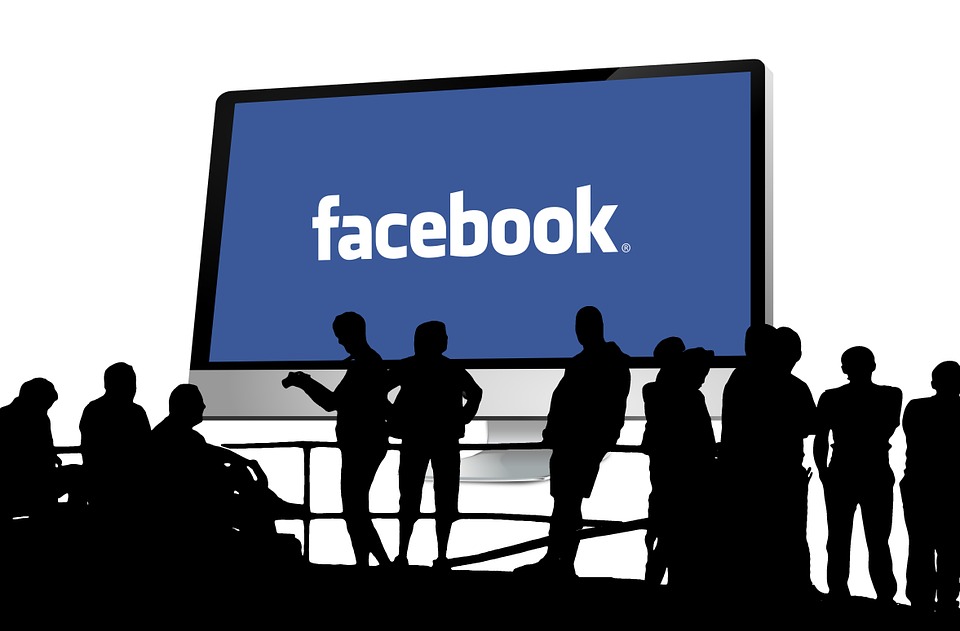 Monitor grande muestra el logo de "facebook". Siluetas de personas observan, simbolizando la conexión social. Marketing digital, red social.