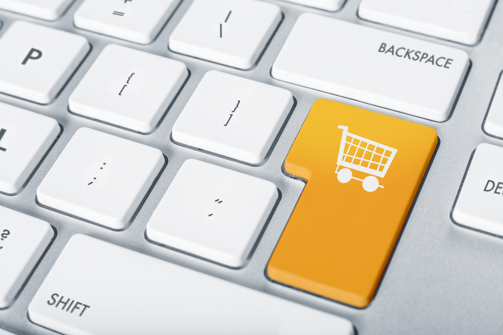 Tecla naranja con carrito de compras destaca en teclado blanco; simboliza comercio electrónico y compra online.