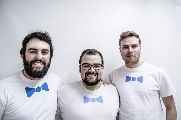 Tres personas sonríen, vistiendo camisetas blancas con pajaritas azules, en un fondo blanco. Marketing de equipo y unidad.