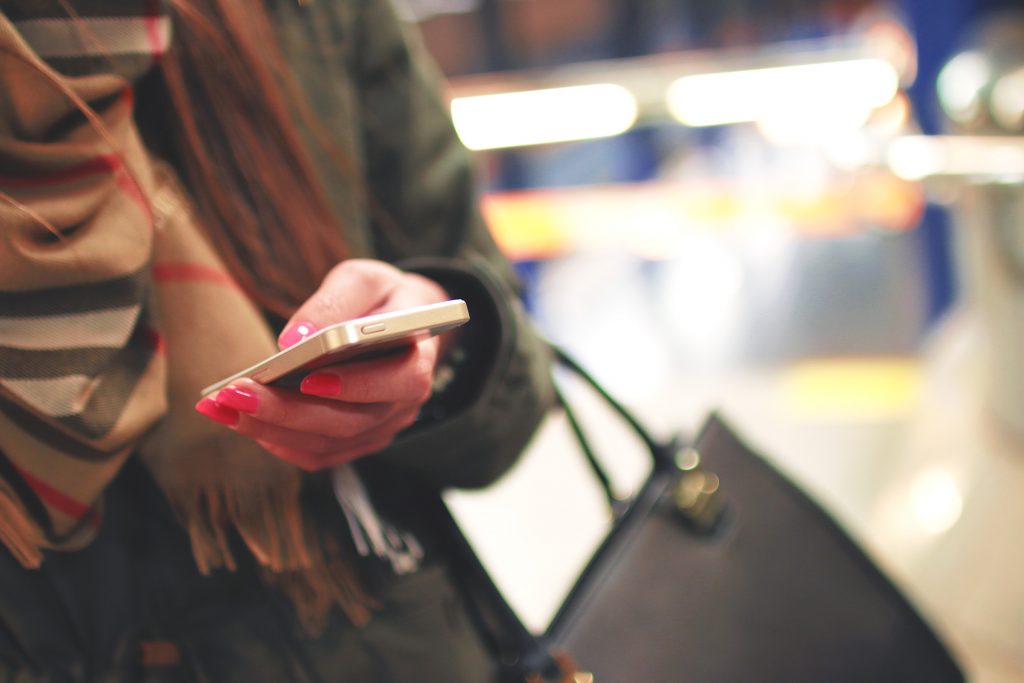 Persona sosteniendo un smartphone, revisando mensajes; lleva una chaqueta y bufanda. Fondo urbano, desenfocado. Tecnología y conectividad móvil.