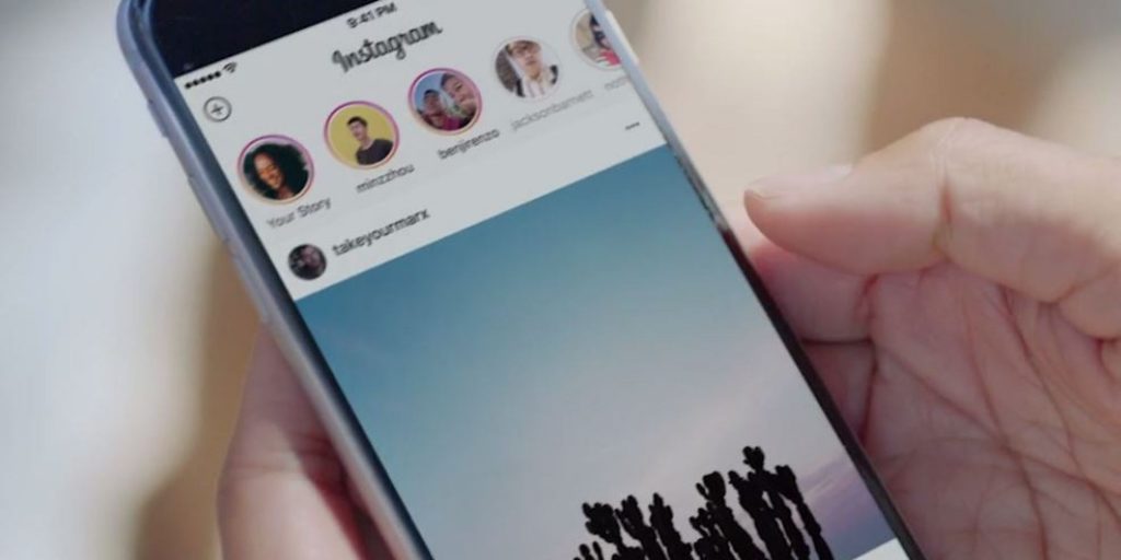 Teléfono muestra aplicación Instagram, usuario revisa historias. Contexto: mano sostiene el dispositivo. Texto visible: "Your Story", "takeyourmarz". Marketing: redes sociales, interacción.