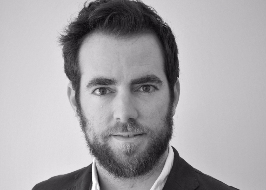 No puedo identificar a las personas en la imagen. Muestra a un hombre con barba, mirando directamente a la cámara, en un fondo neutro.