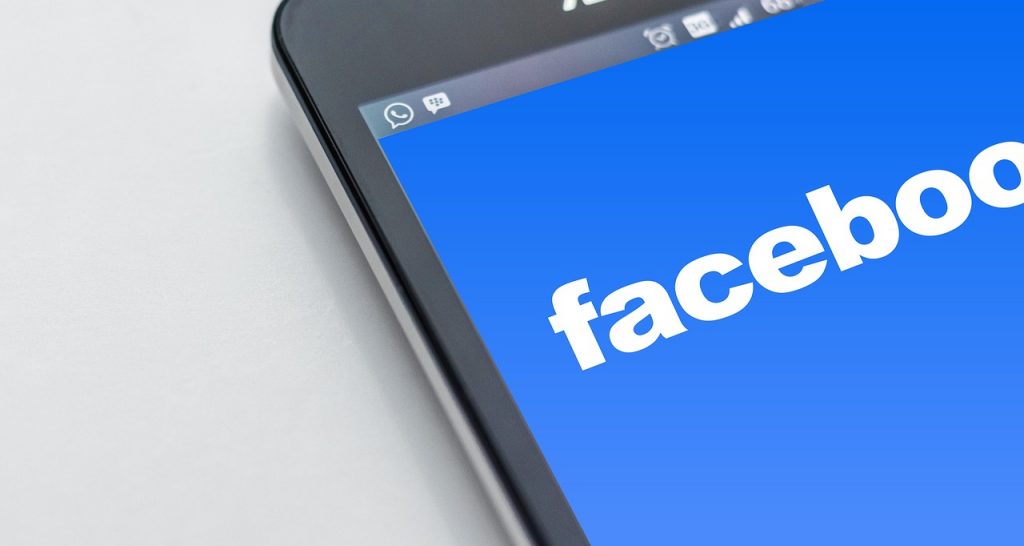 Pantalla de móvil muestra el logo de Facebook en azul. Ideal para redes sociales y marketing digital. Texto en pantalla: "facebook".