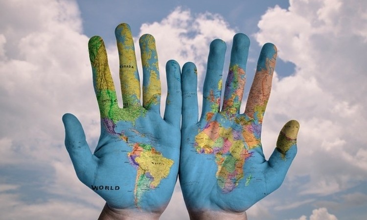 Manos pintadas con mapa del mundo muestran continentes; fondo de cielo nublado. Innovación global.