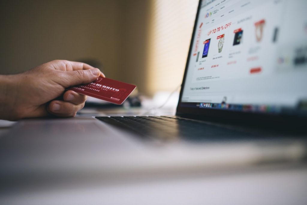 Tarjeta de crédito en mano, usuario realiza compra online en laptop, entorno tranquilo. Texto visible: "UP TO 70% OFF". Ideal para comercio electrónico.