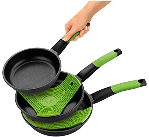 Sartenes negras con mangos verdes apiladas, sostenidas por una mano sobre un fondo blanco. Ideal para cocinas modernas y funcionalidad optimizada.