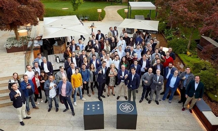 Grupo de personas sonriendo, posando juntas en una terraza al aire libre, rodeadas de árboles y mesas, transmitiendo networking y celebración empresarial.