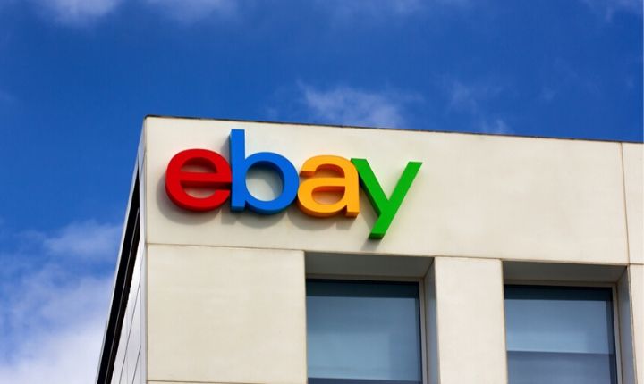 Logotipo de eBay en letras coloridas sobre un edificio blanco moderno; cielo azul de fondo. Marketing digital, comercio electrónico global.