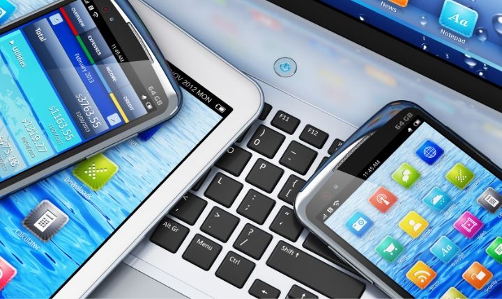 Teléfonos y tablet en teclas de portátil, mostrando aplicaciones coloridas. Contexto tecnológico de conectividad y digitalización.