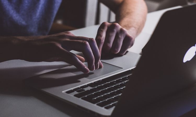Manos escribiendo en un portátil iluminado por una luz suave, simbolizando comunicación digital y productividad en un entorno profesional moderno.
