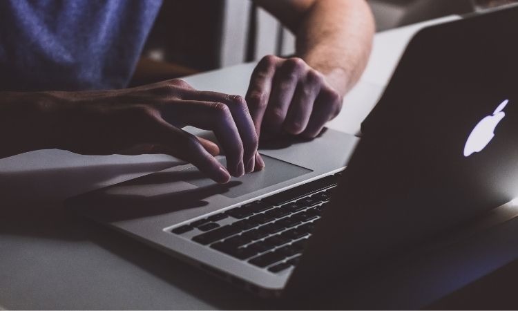Manos tecleando en un portátil Apple, iluminado por la pantalla en un entorno oscuro, transmitiendo concentración y tecnología. Ideal para marketing digital.