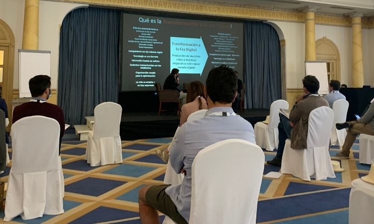 Presentaci&oacute;n en un auditorio con personas sentadas, proyectando diapositiva titulada "&iquest;Qu&eacute; es la Transformaci&oacute;n de la Empresa?". Ambiente de conferencia.