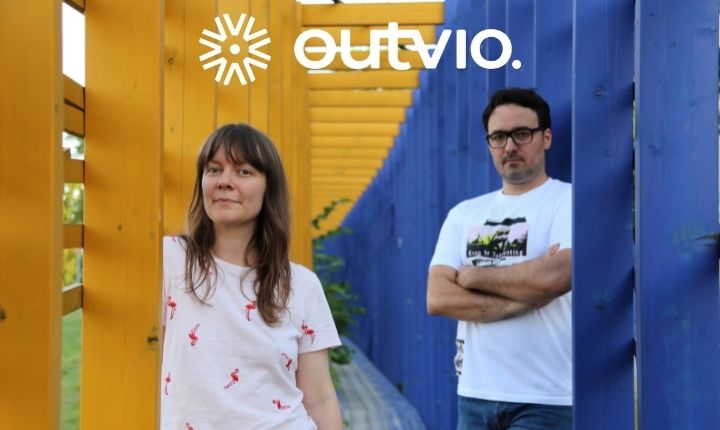 Personas posando; mujer y hombre, junto a estructura amarilla y azul. Logo de "Outvio" arriba. Ideal para marketing y branding visual.