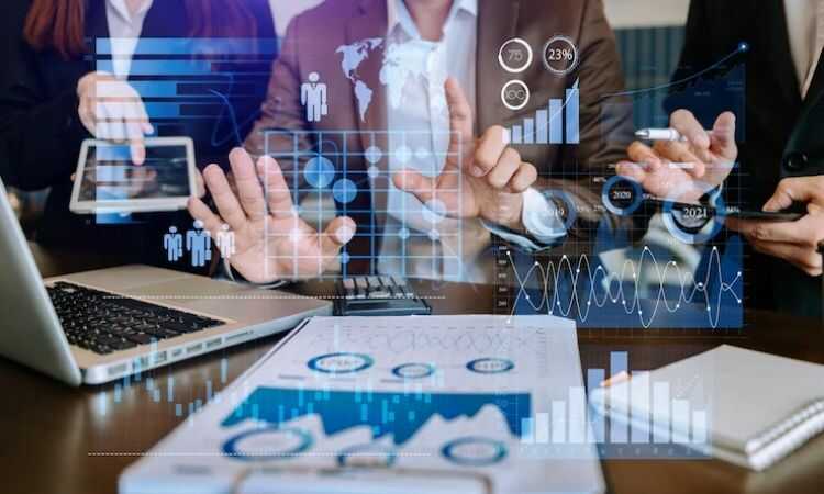 Manos interactuando con gráficos holográficos sobre datos, rodeadas de dispositivos digitales como portátil y tablet en un ambiente de oficina.