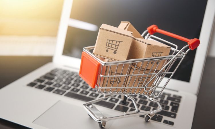 Carrito de compras lleno de cajas sobre un teclado de portátil, encarnando el concepto de compras online y comercio electrónico.