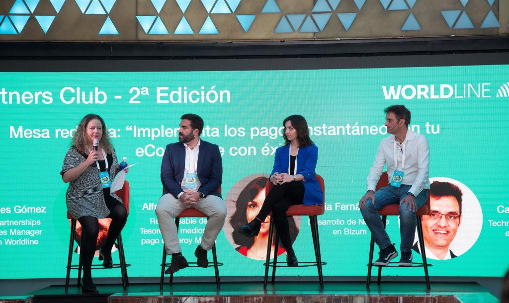 Cuatro personas sentadas, una hablando, en un panel sobre "Implementa los pagos instant&aacute;neos en tu eCommerce con &eacute;xito". Fondo verde con texto de Worldline.