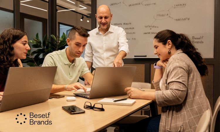 un grupo de trabajo en una oficina con laptops sobre un escritorio y una pizarra con anotaciones