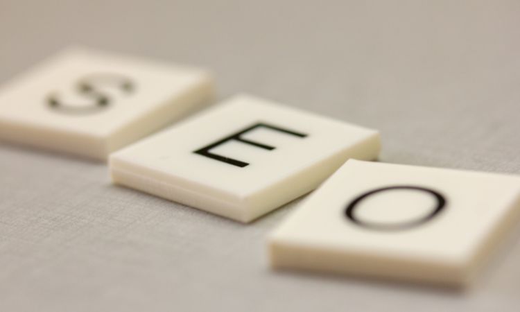 Fichas blancas con letras "S", "E", "O" están dispuestas sobre una superficie gris. Palabras clave: SEO, marketing digital, optimización web.