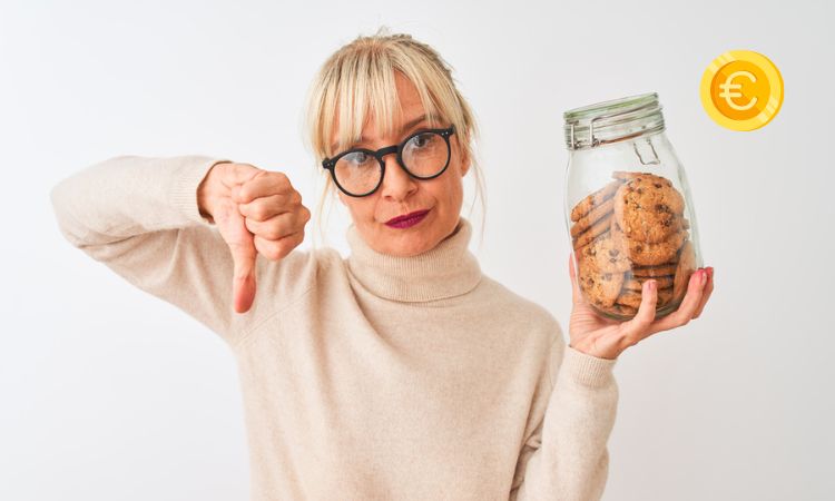 Fotografía de una mujer sosteniendo un tarro de cookies en la mano derecha y haciendo un gesto de desaprobación con el pulgar hacia abajo con la mano izquierda. En la esquina superior derecha aparece una moneda de euro, en referencia a la polémica de elDiario y su opción de cobrar para evitar las cookies