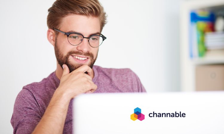 Hombre sonríe mirando portátil, con logotipo de "channable". Contexto de oficina, estantes al fondo. Ideal para marketing digital y tecnología.