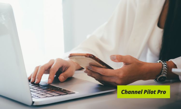 Manos sostienen un móvil mientras teclean en un portátil, contexto de oficina. Texto: "Channel Pilot Pro". Marketing digital y multitarea destacan.