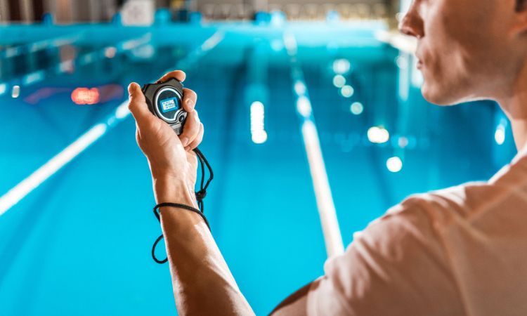 Cron&oacute;metro sujeto por persona mide tiempo en piscina azul. Ambiente deportivo y enfocado en rendimiento. Ideal para marketing deportivo.
