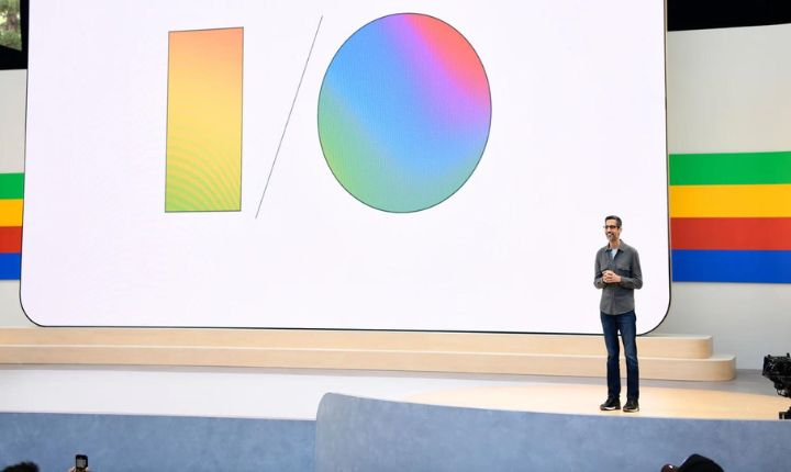 Persona hablando en un escenario con una pantalla grande que muestra un gráfico de I/O colorido, en un evento de tecnología o conferencia.