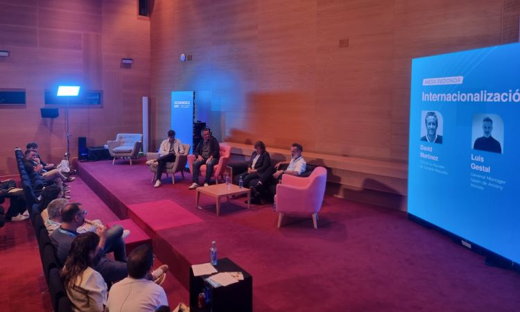 Panelistas sentados discuten internacionalizaci&oacute;n en escenario con alfombra roja; pantalla muestra "Internacionalizaci&oacute;n," "David Mart&iacute;nez," "Luis Gestal." P&uacute;blico atento.