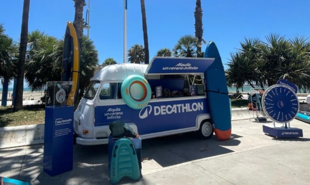 Fotografía de la experiencia organizada por Decathlon en La Malagueta. En la imagen se ve una furgoneta brandeada rodeada de artículos deportivos acuáticos