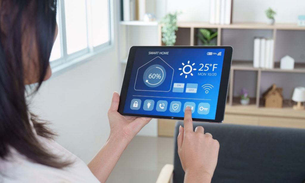 Persona controlando un sistema de domótica desde una tablet, gestionando temperatura, seguridad y dispositivos inteligentes en el hogar.