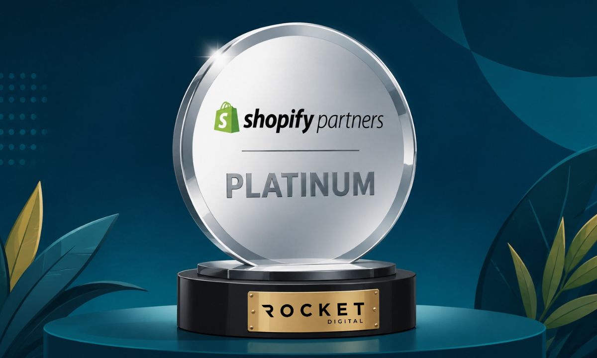 Imagen de un trofeo redondo, de diseño elegante y color platino brillante. En el trofeo se ve el logo de shopify partners y pone "PLATINUM" debajo. En el pie del trofeo, en una placa dorada, se ve el logo de Rocket Digital.